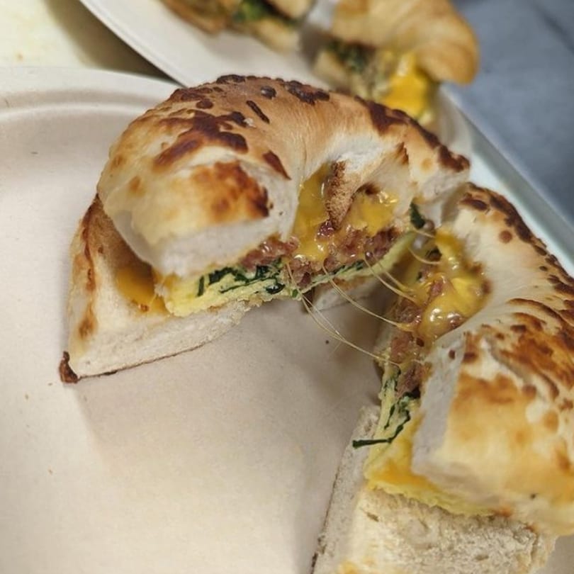 A sliced bagel sandwich with melted cheese, egg, and spinach, showing a cheese pull.