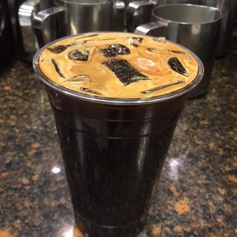 Close-up of a Grouchy John's Coffee iced coffee with ice cubes and a creamy top layer.